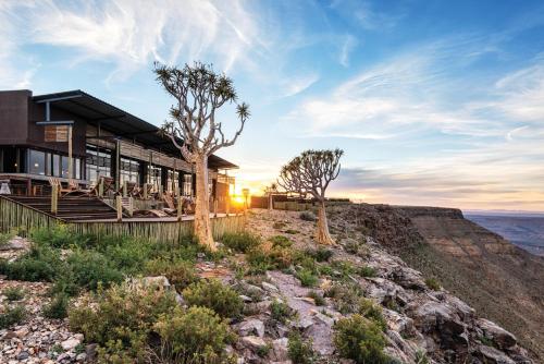 a house on top of a mountain with the sun setting at Fish River Lodge in Ariamab