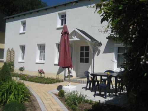 une maison blanche avec une table et un parapluie rouge dans l'établissement Pension Waldrose, à Sellin