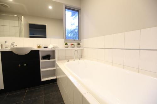 a white bathroom with a tub and a sink at Lorne Luxury in Lorne