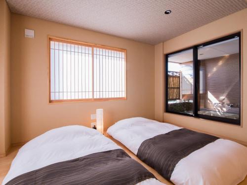 two beds in a room with a window at Dogo Onsen Yachiyo in Matsuyama