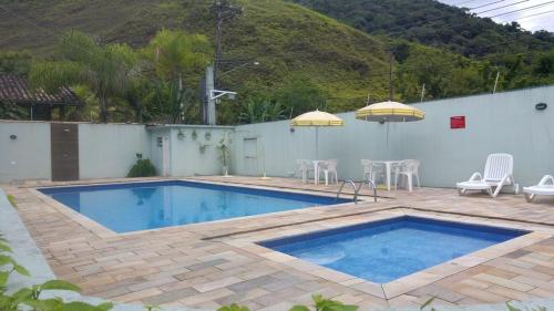 einen Pool mit Stühlen, einem Tisch und einem Sonnenschirm in der Unterkunft Casa Condominio Fechado Total Segurança - Juquehy in Juquei