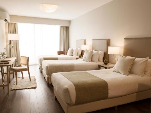 ブエノスアイレスにあるDazzler by Wyndham Poloのベッド3台、テーブル、椅子が備わるホテルルームです。