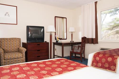 a hotel room with a bed and a television and a chair at Red Carpet Inn and Suites Plymouth in Plymouth