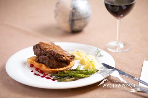 a plate of food with meat and vegetables and a glass of wine at Pensiunea Ecaterina in Berzasca