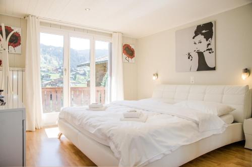 a white bedroom with a large white bed and a window at Chalet D in Grindelwald