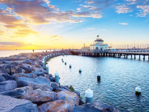 a pier with a lighthouse in the water at sunset at Beachfront Apartment in Melbourne
