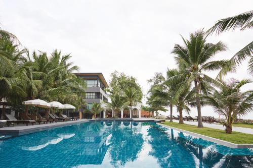 a swimming pool with palm trees and a building at Siambeach Resort in Cha Am