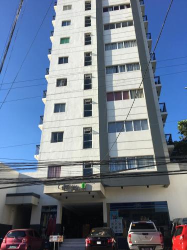 a tall white building with cars parked in front of it at Simply Comfy 916 (Cityscape Bacolod) in Bacolod