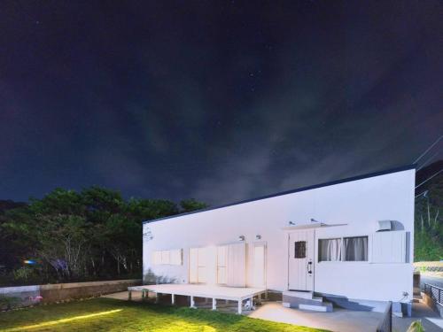 a white building with a bench in a yard at night at Amami Mahalo in Tatsugo