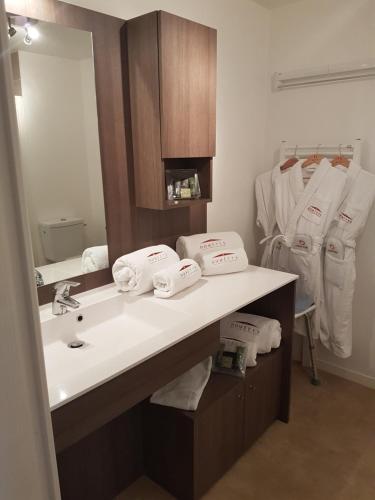 La salle de bains est pourvue d'un lavabo, d'un miroir et de serviettes. dans l'établissement Domitys Le Carrousel, à Cabourg