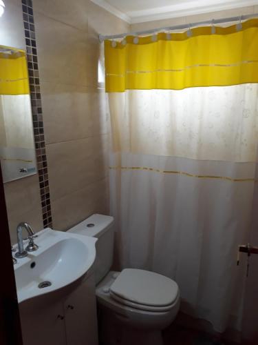 un baño con un aseo blanco y una cortina de ducha amarilla en el Hotel La Palmera de Villa Gesell