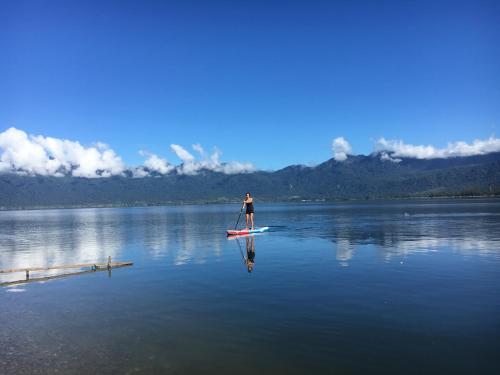 a man standing on a paddle board on a lake at Eka's Bungalows in Maninjau