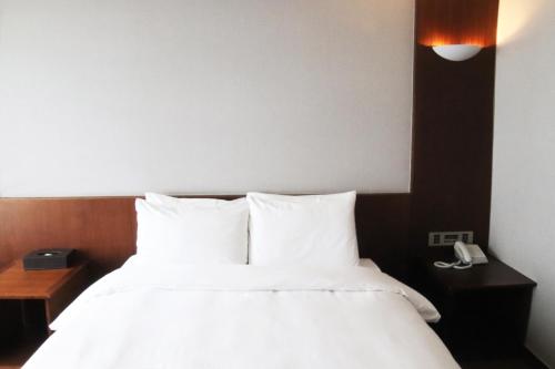 a bedroom with a bed with white sheets and a phone at Mstay Hotel in Seogwipo