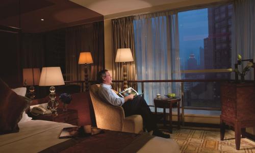 a man sitting in a chair reading a book in a hotel room at Chengdu Tianfu Sunshine Hotel in Chengdu