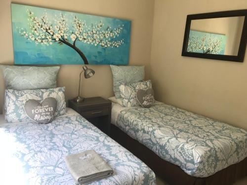 two beds in a room with a painting on the wall at Bay Breeze Guesthouse in Gordonʼs Bay