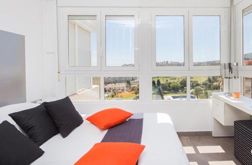 Una cama blanca con almohadas naranjas en una habitación con ventanas. en La Colina, en Torremolinos