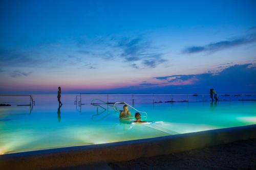 a person sitting in a swimming pool at night at Aminess Planet Camping Holiday Homes Maravea in Novigrad Istria
