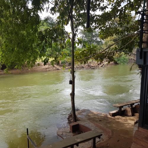 a river with two picnic tables next to a tree at Kaengkrachan River Hut in Kaeng Krachan