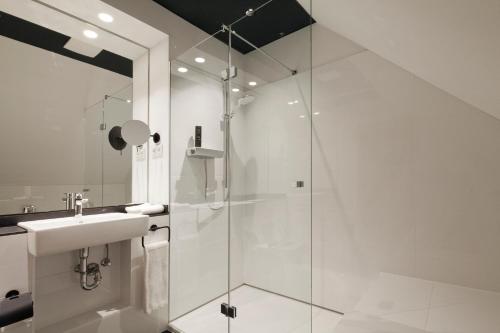 a white bathroom with a shower and a sink at Schulhaus Hotel in Schwelm