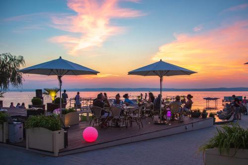 people sitting at tables under umbrellas on the beach at sunset at Mala Garden Design Hotel in Siófok