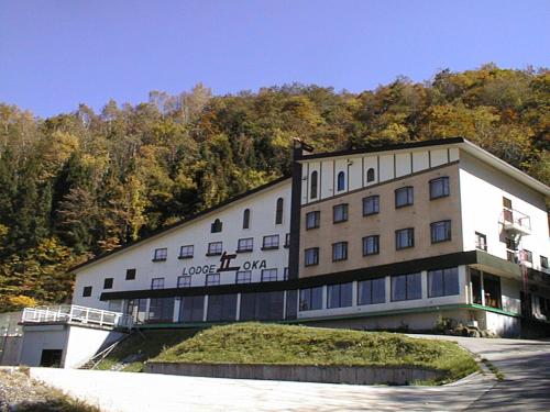 a building with a grassy hill in front of a mountain at Naeba Lodge Oka in Yuzawa