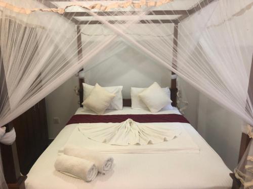 a bedroom with a canopy bed with white sheets and pillows at Villa Red Lobster in Hikkaduwa