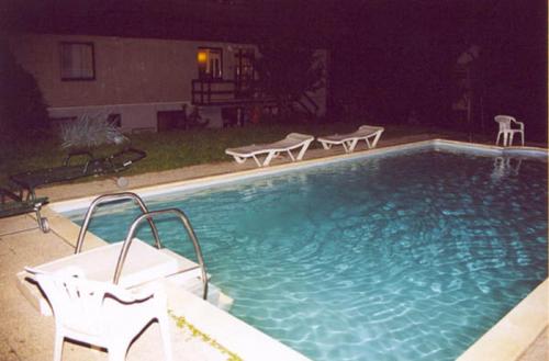 a swimming pool at night with two white chairs in it at Herold Panzió in Dunabogdány