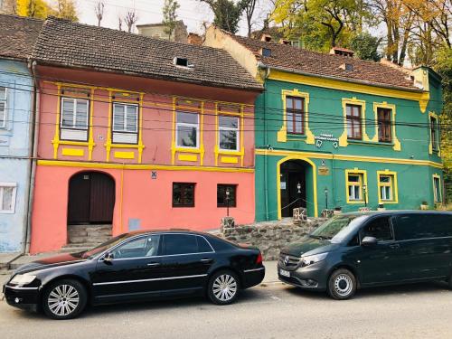 dos autos estacionados frente a una casa colorida en V. Apartment, en Sighişoara