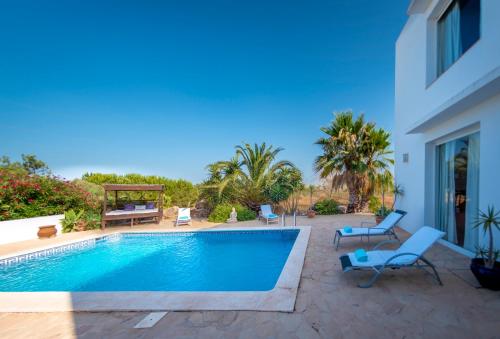 a swimming pool in a yard with chairs and a house at Villa Can Massaueta in Sant Jordi