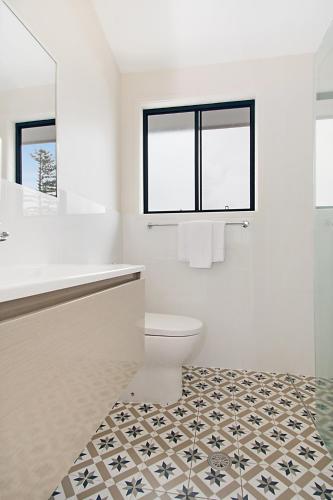 a white bathroom with a toilet and a window at Gosamara Apartments in Byron Bay