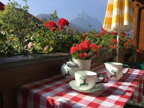 a table with a table cloth with cups and flowers at Almroeserl in Mittenwald