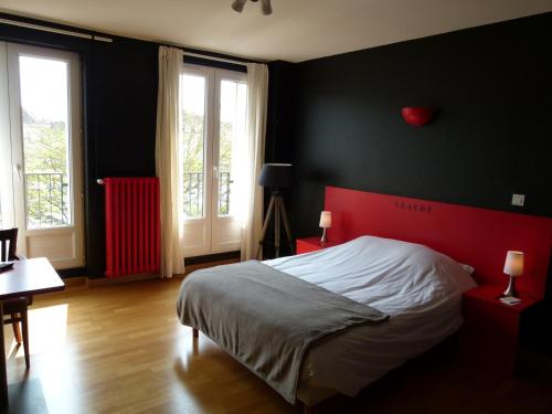 a bedroom with a bed with a red headboard and two windows at Hôtel Victor in Beauvais
