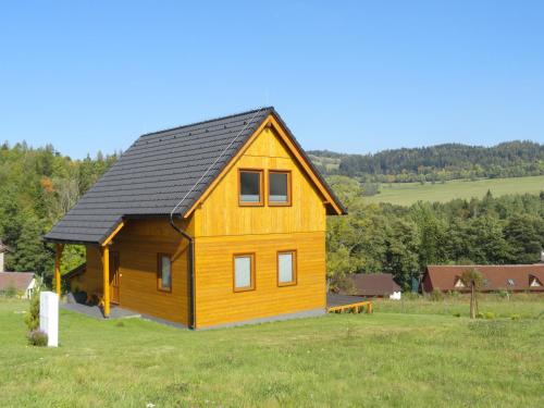 a wooden house with a black roof in a field at Chata Karamelka in Dolní Moravice
