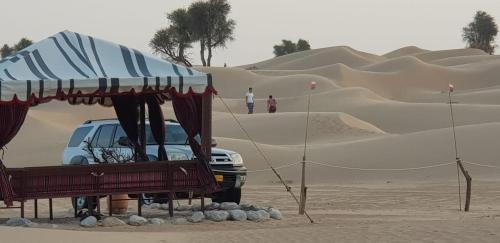 un coche aparcado en el desierto cerca de unas dunas de arena en Legend Desert camp, en Fulayj al Mashāʼikh