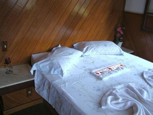 a bed with white sheets and a book on it at Pousada Recanto das Águas in Lumiar