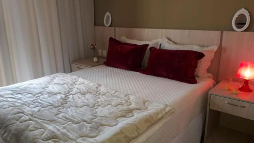 1 dormitorio con 1 cama blanca grande con almohadas rojas en Flat no Aldeia das Águas (Deluxe), en Barra do Piraí