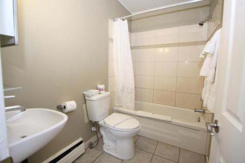 a bathroom with a toilet and a tub and a sink at Harrison Spa Motel in Harrison Hot Springs
