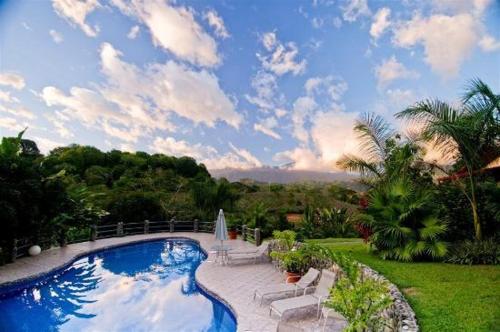 ein Schwimmbad in einem Garten mit wolkigem Himmel in der Unterkunft Blue Banyan Inn in Quepos