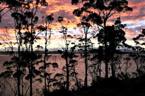 a sunset over a body of water with trees at Baragoola Retreat - Luxury Waterfront Property in Sandford