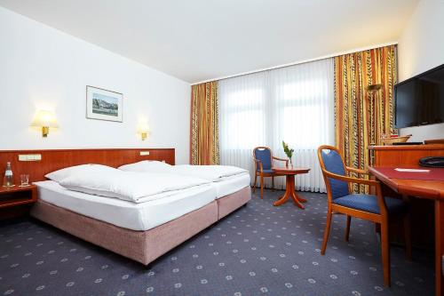 Habitación de hotel con cama, escritorio y TV. en Trans World Hotel Columbus, en Seligenstadt