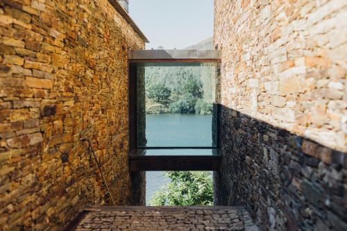 a window in a brick wall with a view of a river at Octant Douro in Castelo de Paiva