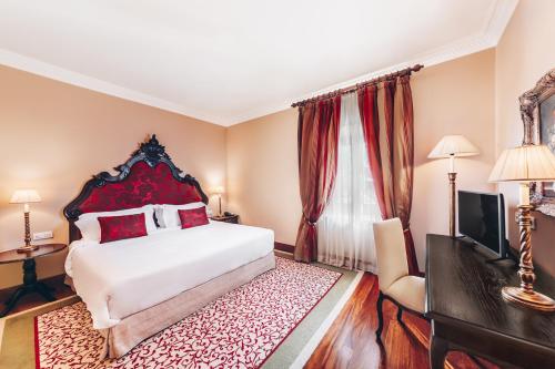 a bedroom with a bed and a desk and a television at Convento do Espinheiro, Historic Hotel & Spa in Évora