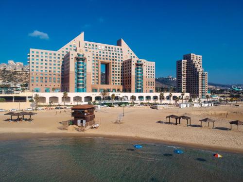 a beach with a large building and some water at Almog Beach Apartments מגדלי חוף הכרמל חיפה in Haifa