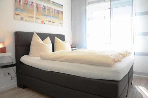 ein Bett mit weißer Bettwäsche und Kissen in einem Schlafzimmer in der Unterkunft Suite Gartenstraße im hellen Ambiente in Norderney