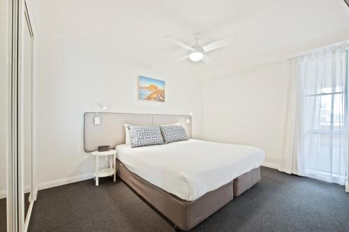 a white bedroom with a bed and a ceiling fan at Quest Newcastle in Newcastle
