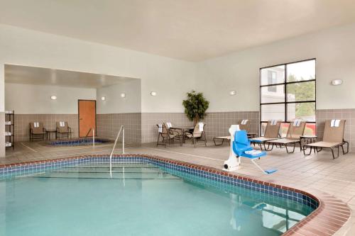 una piscina en una habitación de hotel con sillas y mesas en Wingate by Wyndham Parkersburg - Vienna, en Parkersburg