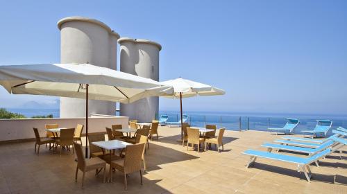 a patio with tables and chairs and umbrellas and the ocean at Villa Angelina in Massa Lubrense