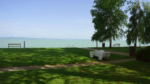 two white chairs sitting in a park near the water at Hotel Lido in Siófok