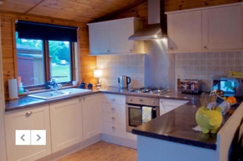 a kitchen with white cabinets and a sink and a window at Caol Gleann Lodge in Rowardennan