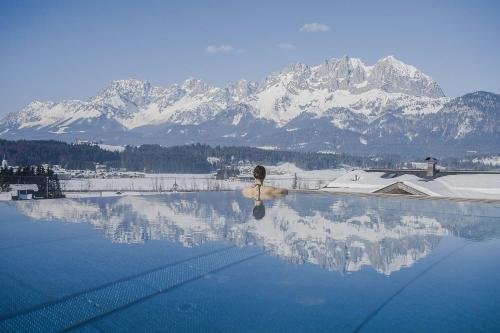 a woman sitting in a pool with mountains in the background at Appartements am Römerweg in Oberndorf in Tirol
